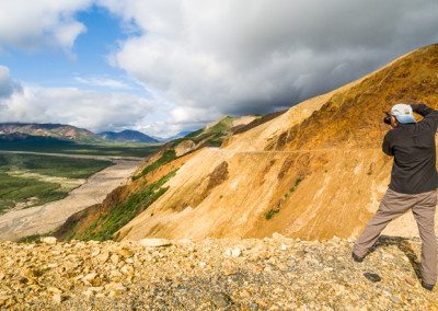 Photographer and Polychrome Pass. The name comes from the colorful ciffs along the park road in the background on right. Denali National Park, Alaska.
